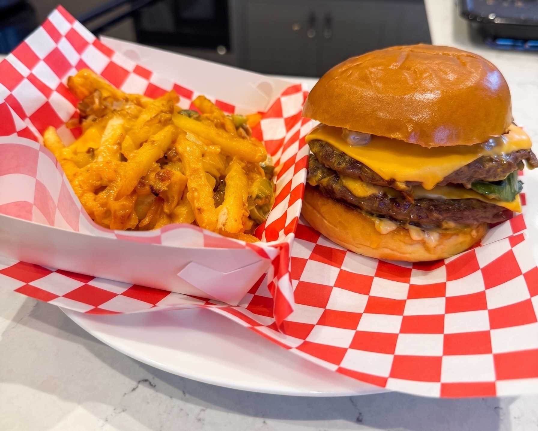 A mustard-grilled double-double cheeseburger with fresh tomato and lettuce next to a tray of loaded animal-style fries with melted cheese and caramelized onions.